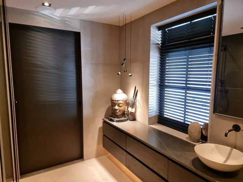 Badkamer met een zwevend donker badmeubel, een witte waskom, zandkleurige wandtegels en een donkere deur naast het raam.
