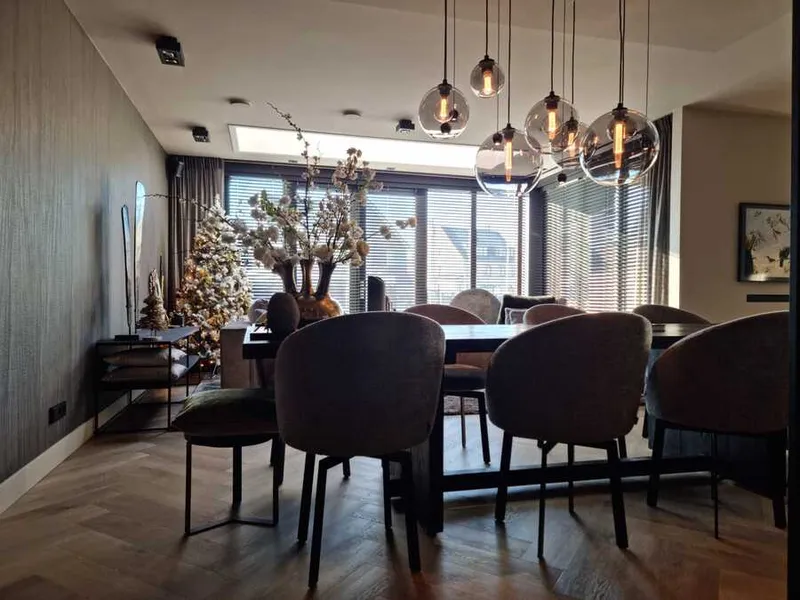 Eetkamer met een lange donkere tafel, ronde stoelen, glazen hanglampen en een wand met gestructureerd behang.