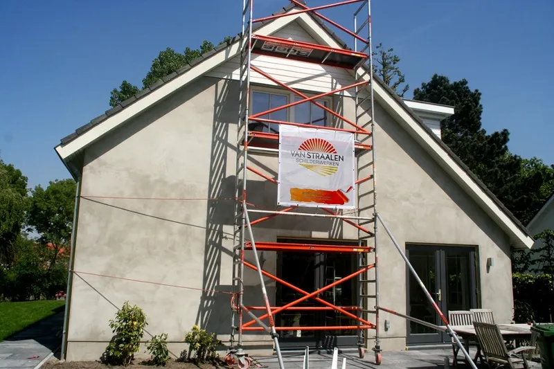 Woonhuis met een gestucte gevel en een rolsteiger tegen de puntgevel, met een doek van Van Straalen Schilderwerken aan de steiger.