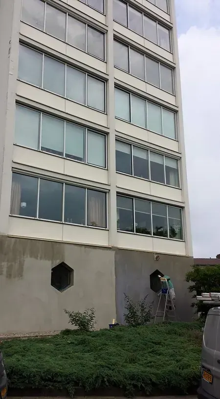 Hoog gebouw met een gestucte onderbouw met zeshoekige ramen; tegen de gevel staat een ladder.