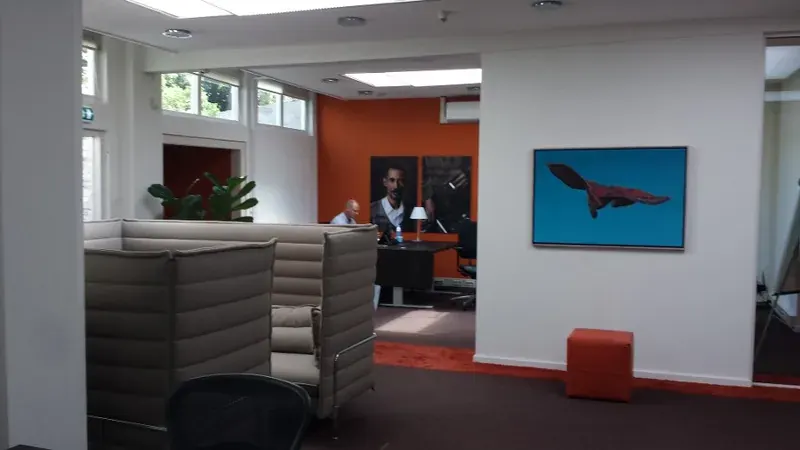Kantoorruimte na het latexen: witte wanden en plafond, een oranje accentwand en een kunstwerk aan de muur.