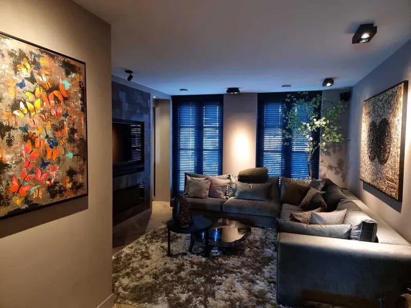 Woonkamer in donkere tinten met een grote hoekbank, een donkere schouw en kleurrijke kunst aan een lichte wand.