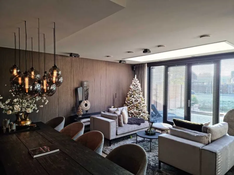 Woonkamer in december met een bruine wand met structuur, glazen hanglampen boven de eettafel en een kerstboom voor de schuifpui.